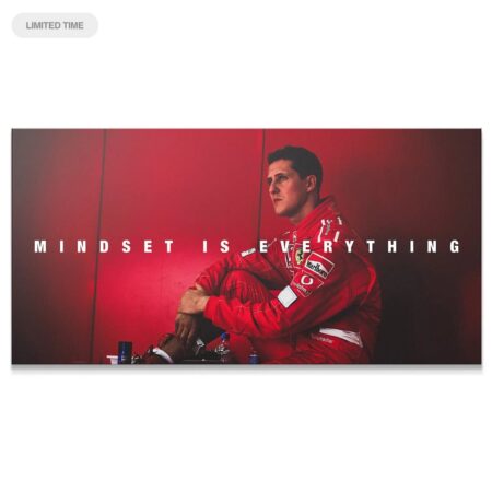 Wide shot of Michael Schumacher sitting against a red wall with the quote 'Schumacher - Mindset Is Everything' overlaid.