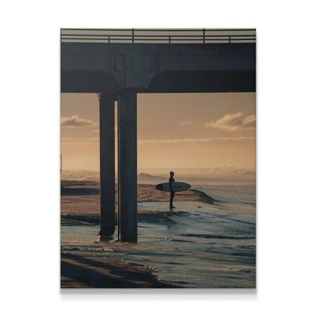 Full vertical photographic print showing a surfer silhouette under concrete pier structure in 'The Morning Wait'.