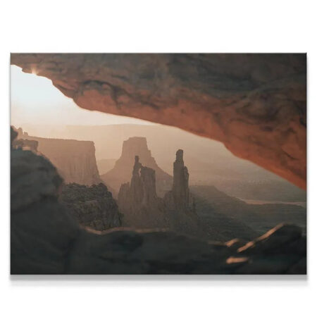 Wide view of desert spires framed by a natural arch at sunrise, titled Under the Glow.